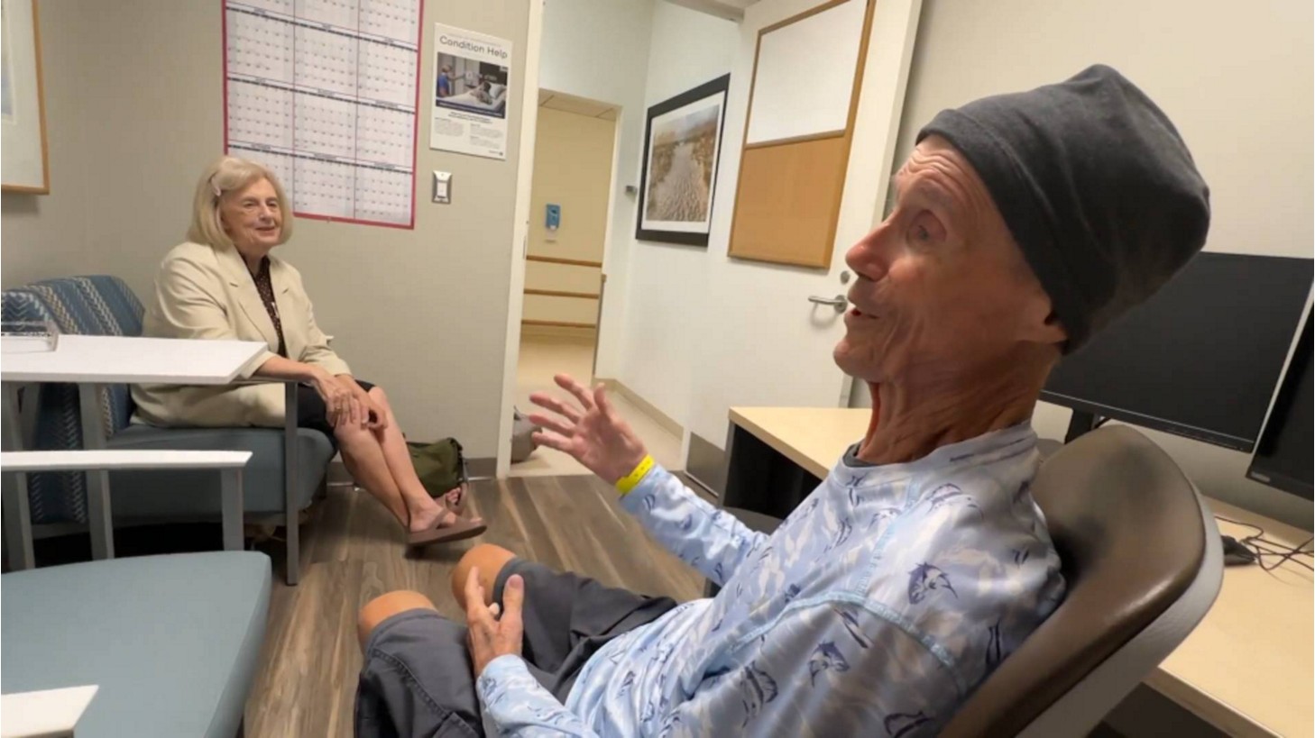 Patient Richard Martin speaking in a clinic room while his wife, Arlene Bouchard, listens